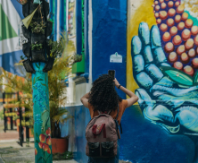 Fotografía de una joven tomando una fotografía con su celular a un mural de la Candelaria de Bogotá